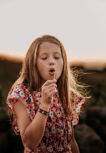 child outside blowing a dandelion